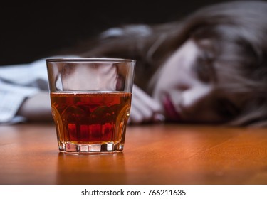Young woman in depression, drinking alcohol on dark background. Focus on the glass