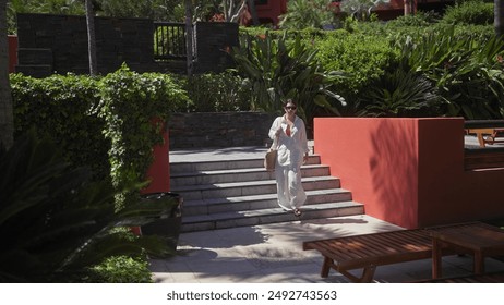 A young woman descends steps at a tropical balinese resort surrounded by lush greenery. - Powered by Shutterstock