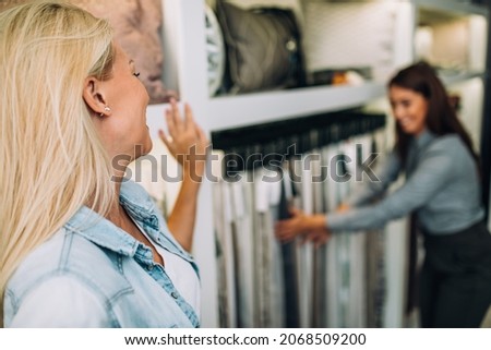 Young woman designer talking with a saleswoman and chooses fabrics for curtains in textile show room.