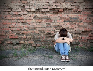 Young woman in despair sitting against a brick wall - Shutterstock ID 129019094