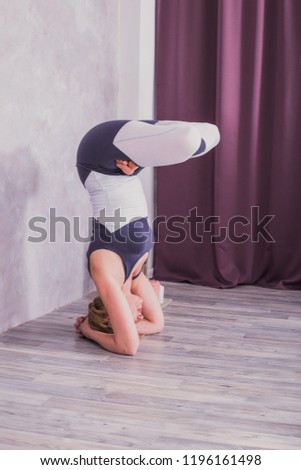 Young woman in difficult yoga asanas in sports jumpsuit practicing yoga asanas at home. Athlete performs handstands