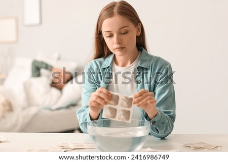 Young woman dipping mustard plaster into bowl of water in bedroom