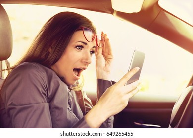 Young Woman Distracted Reading A Message On Cellphone, Amazed, While Driving A Car  