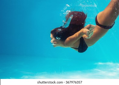 young woman dive in pool, profile, shot through the glass of the pool