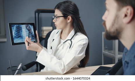 Young woman doc explaining chest x-ray results to male patient showing it on tablet - Powered by Shutterstock