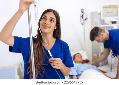 Young woman doctor anesthesiologist dressed in blue gown, puts the IV dropper in hospital room - Powered by Shutterstock