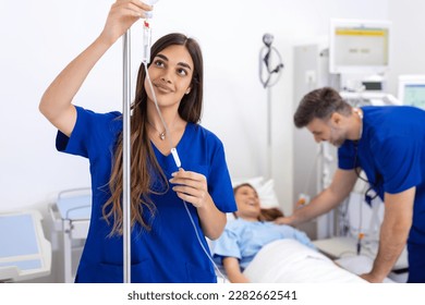 Young woman doctor anesthesiologist dressed in blue gown, puts the IV dropper in hospital room - Powered by Shutterstock