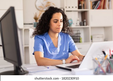 Young Woman Doctor Assistant Working In Medical Office Using Laptop Computer And Writing Prescription