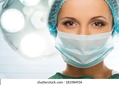 Young woman doctor in cap and face mask in surgery room interior