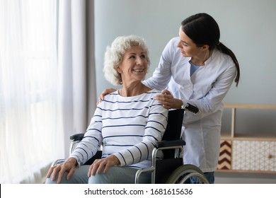 Young woman doctor give help support handicapped old lady patient sitting in wheelchair, female caregiver or nurse assist take care of smiling senior disabled grandma, elderly healthcare concept