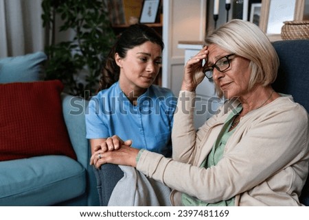 Young woman doctor health care worker medic nurse comforting older senior woman at home visit, patient suffering from clinical depression and anxiety. Sick adult female in home-care program