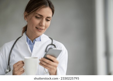 Young woman doctor holding her smartphone. Female doctor with smartphone working at the office. - Powered by Shutterstock