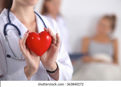 Young Woman Doctor Holding A Red Heart, Standing On Gray Background