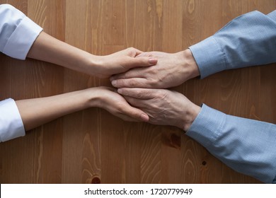 Young woman doctor, nurse or caregiver holding hands of senior old man patient having parkinson geriatric disease. Gerontology, elder people health care responsibility concept. Close up top view.