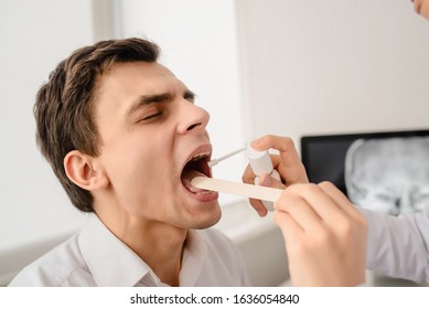 Young Woman Doctor Otolaryngologist Examine Patient Larynx And Oral Cavity And Spray With Antiseptic Spray. Tonsillitis Treatment