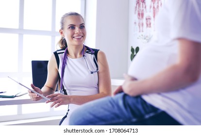 Young woman doctor with stethoscope speaking with pregnant woman at hospital.
