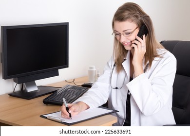 Young woman doctor talking by phone and writing something in her office