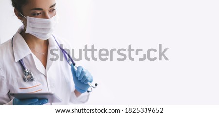 Young woman doctor wearing protective mask and latex gloves holding stethoscope and tablet isolated on white background. Place for text.