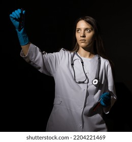 Young Woman Doctor In A White Coat And Medical Gloves Holds Test Tubes With Blood In Her Hands On A Black Background