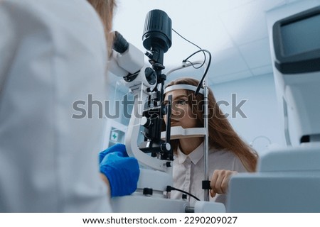 A young woman at a doctor's appointment. An optometrist examines the patient's vision using a slit lamp.