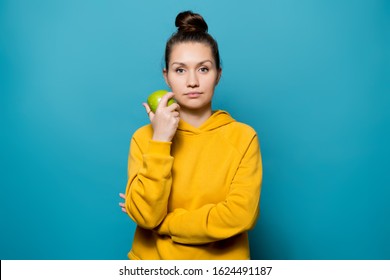 Young Woman Does Not Express Any Emotions And Holds An Apple Near Her Face