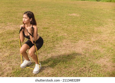 A young woman does a set of resistance band squats. Tube bands with foam handle equipment. Outdoor leg workout.