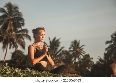 Young woman does yoga for healthy lifestyle on sea beach at palm trees background. Female performing sports exercises to restore strength and spirit. Yoga position on tropical climate - Powered by Shutterstock