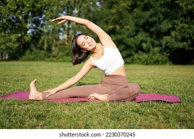 Young woman does yoga on lawn in park, stretching on fitness mat, wellbeing concept. - Powered by Shutterstock