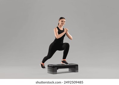 Young woman doing aerobic exercise with step platform on light background - Powered by Shutterstock