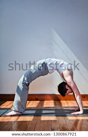 A young woman doing a back bend on an exercise mat in a sun-filled room.