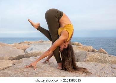 Young woman doing balance yoga asana on a rock near the sea. Variation of forward fold, uttanasana.