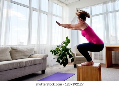Young woman doing box jump exercise in living room at home, copy space. Jumping squats, side view. Sport, healthy lifestyle concept 