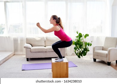 Young woman doing box jump exercise in living room at home, copy space. Jumping squats. Sport, healthy lifestyle concept 