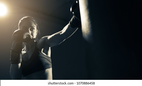Young woman doing boxing training at the gym, she is wearing boxing gloves and hitting the punching bag - Powered by Shutterstock