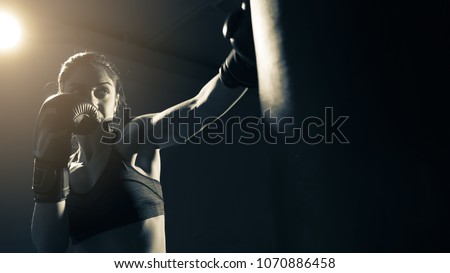 Young woman doing boxing training at the gym, she is wearing boxing gloves and hitting the punching bag