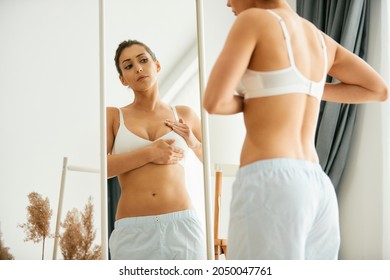 Young woman doing breast self-examination while looking herself in a mirror at home. - Shutterstock ID 2050047761