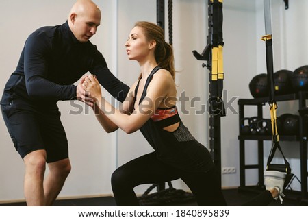 Young woman doing CrossFit suspension training with her personal trainer or coach in a sports club. Private fitness workout. The concept of weight loss and gaining muscle mass.