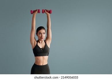 Young Woman Doing Dumbbell Workout , Working On Arms Strength, Looking At Copy Space. Smiling Athletic Lady Lifting Pink Fitness Dumbells Up Over