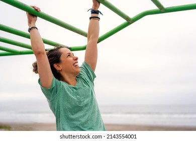 Young Woman Doing Excercise On Hanging Pull Up Bar Outdoors On The Beach