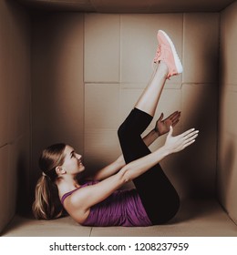 Young Woman Doing Exercises In Cardboard Box. Young Smiling Girl. Life In Little Cardboard Box. Uncomfortable Life. Personal Spase Concepts. Young Introvert. Sports And Healthy Lifestyle.