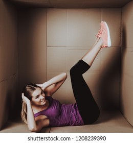 Young Woman Doing Exercises In Cardboard Box. Young Smiling Girl. Life In Little Cardboard Box. Uncomfortable Life. Personal Spase Concepts. Young Introvert. Sports And Healthy Lifestyle.