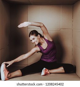 Young Woman Doing Exercises In Cardboard Box. Young Smiling Girl. Life In Little Cardboard Box. Uncomfortable Life. Personal Spase Concepts. Young Introvert. Sports And Healthy Lifestyle.