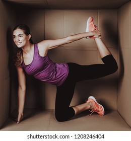 Young Woman Doing Exercises In Cardboard Box. Young Smiling Girl. Life In Little Cardboard Box. Uncomfortable Life. Personal Spase Concepts. Young Introvert. Sports And Healthy Lifestyle.