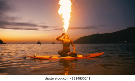 Young woman doing fireshow fire breathing perforrmance on sup board with paddle at sunset. - Powered by Shutterstock