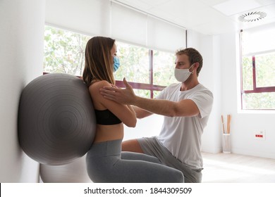 Young Woman Doing Fitness Ball And Pilates Exercise With Coach Wearing Mask During Covid-19