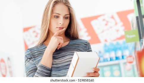 Young Woman Doing Grocery Shopping At The Supermarket And Reading A Food Label With Ingredients On A Box, Shopping And Nutrition Concept