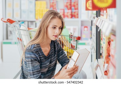 Young woman doing grocery shopping at the supermarket and reading a food label with ingredients on a box, shopping and nutrition concept