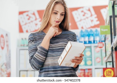 Young Woman Doing Grocery Shopping At The Supermarket And Reading A Food Label With Ingredients On A Box, Shopping And Nutrition Concept