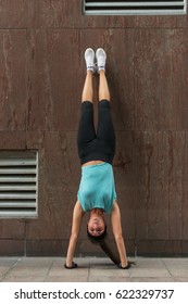 Young woman doing handstand exercise against the wall on the city street.