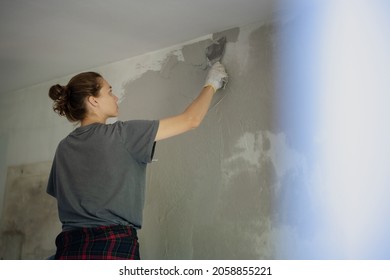 Young woman doing home repairs by applying plaster using a trowel